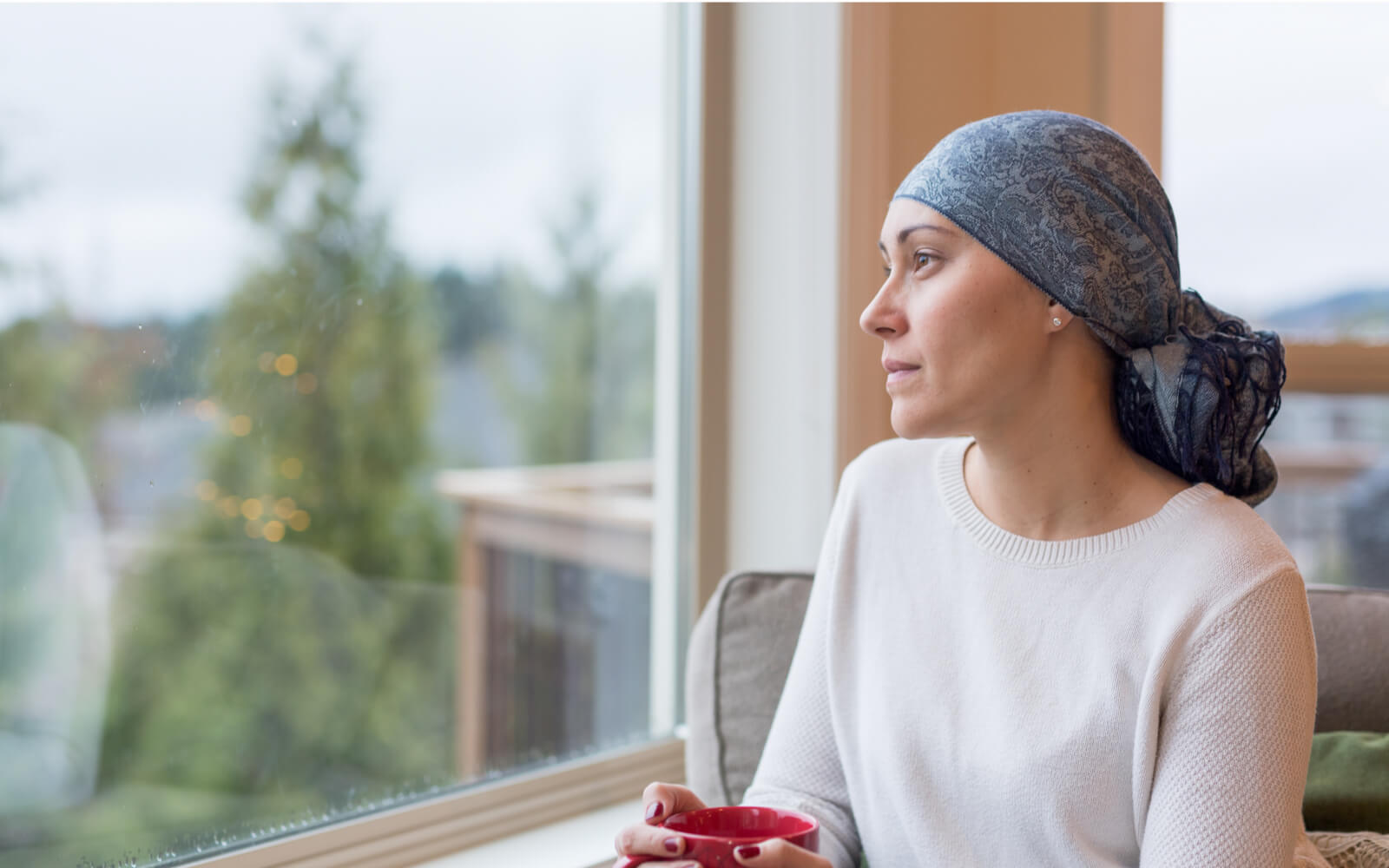 woman with cancer drinks a cup of tea and looks out the window
